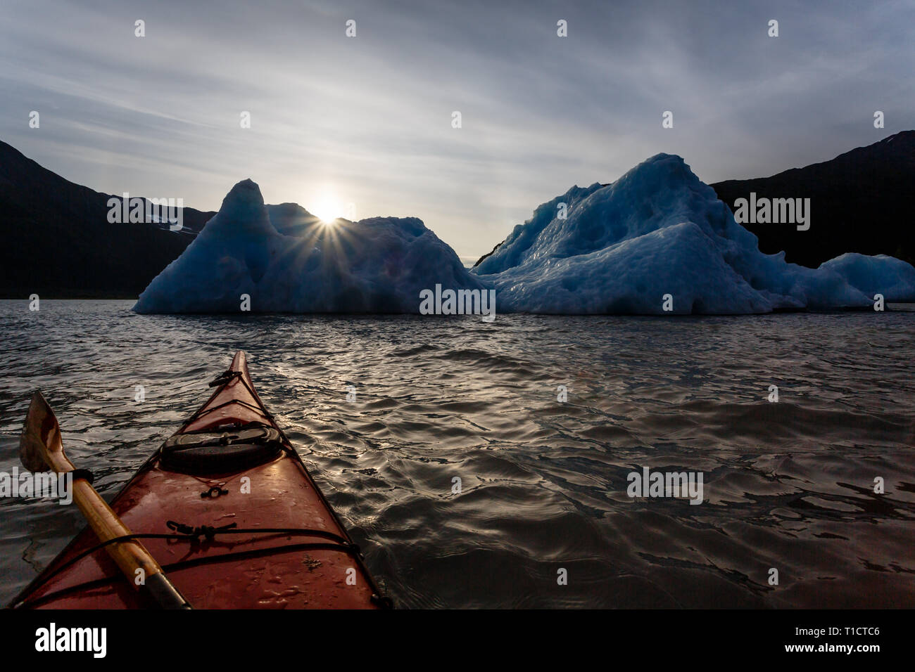 Kayak approaching near turquoise blue icebergs at sunrise Stock Photo
