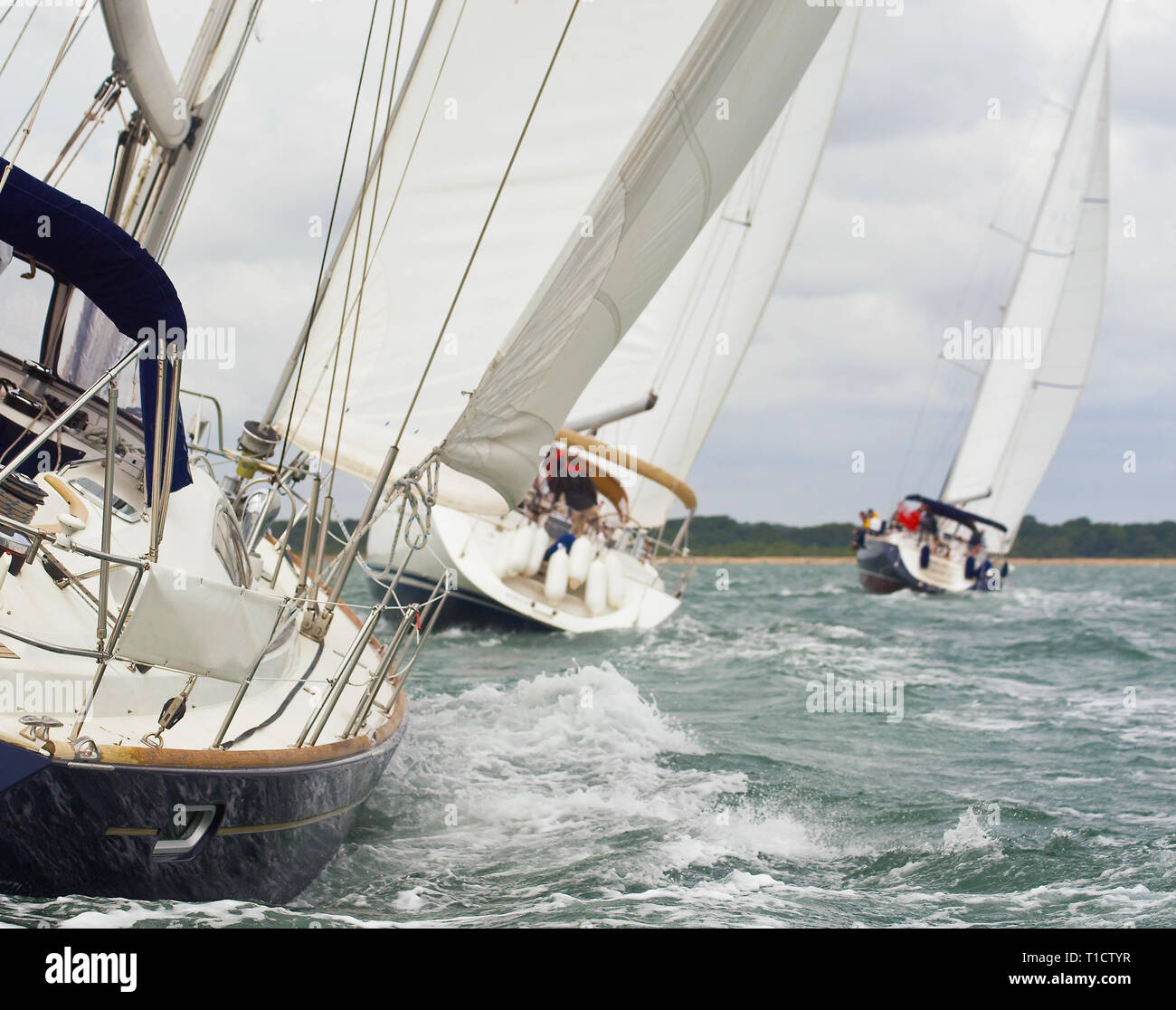 Three beautiful yachts sailboats with white sails racing close to each other on a bright sunny day Stock Photo