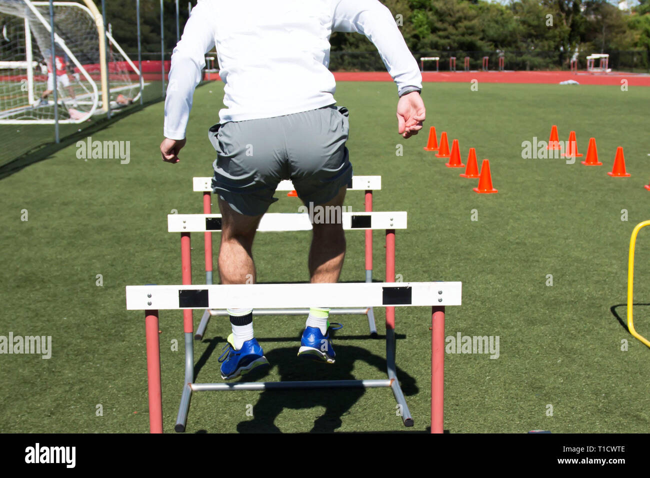 A high school male athlete jumps over hurdles during strength training