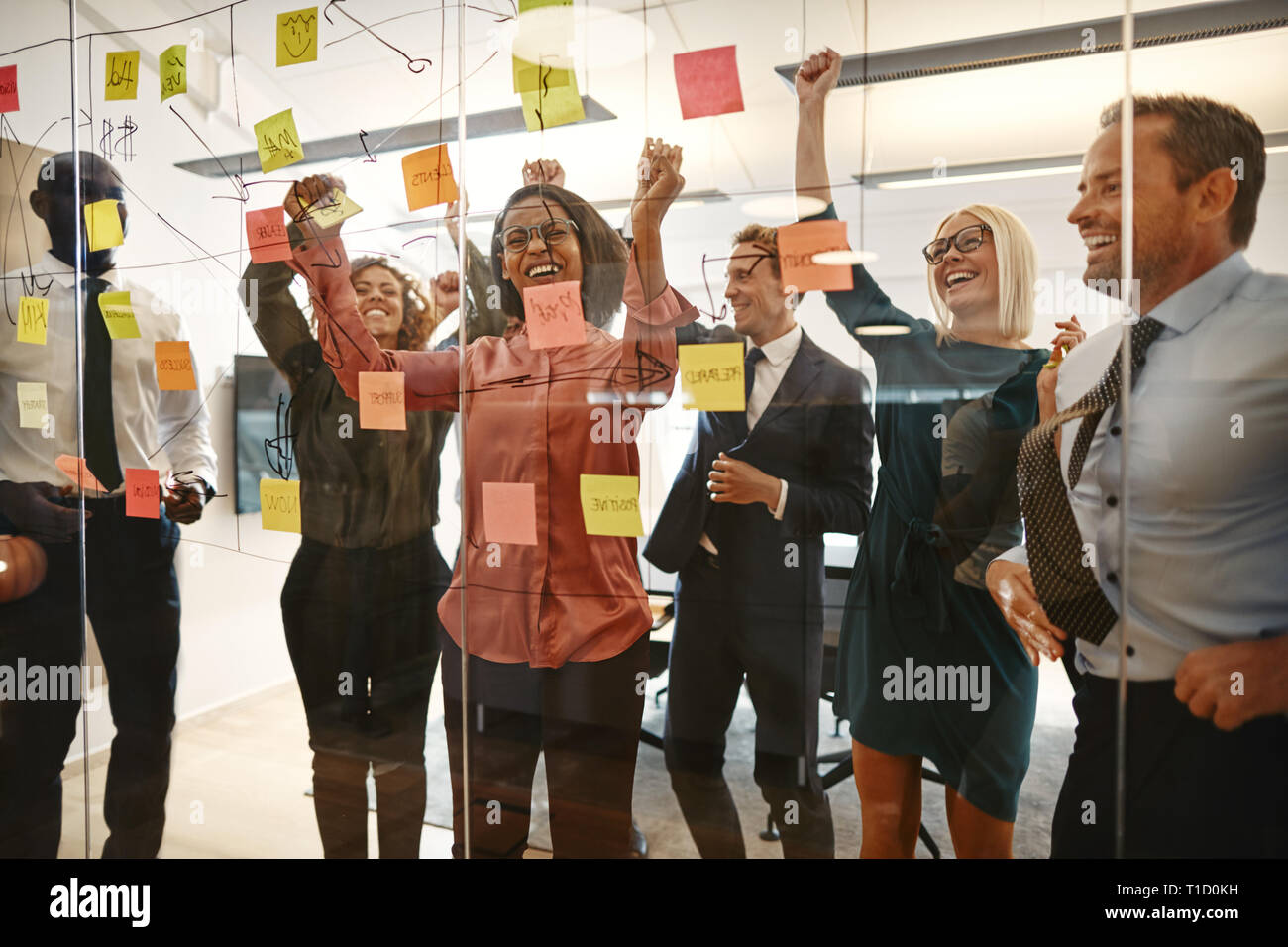 Cheering group of excited businesspeople jumping up and down while celebrating after a brainstorming session with sticky notes in an office Stock Photo