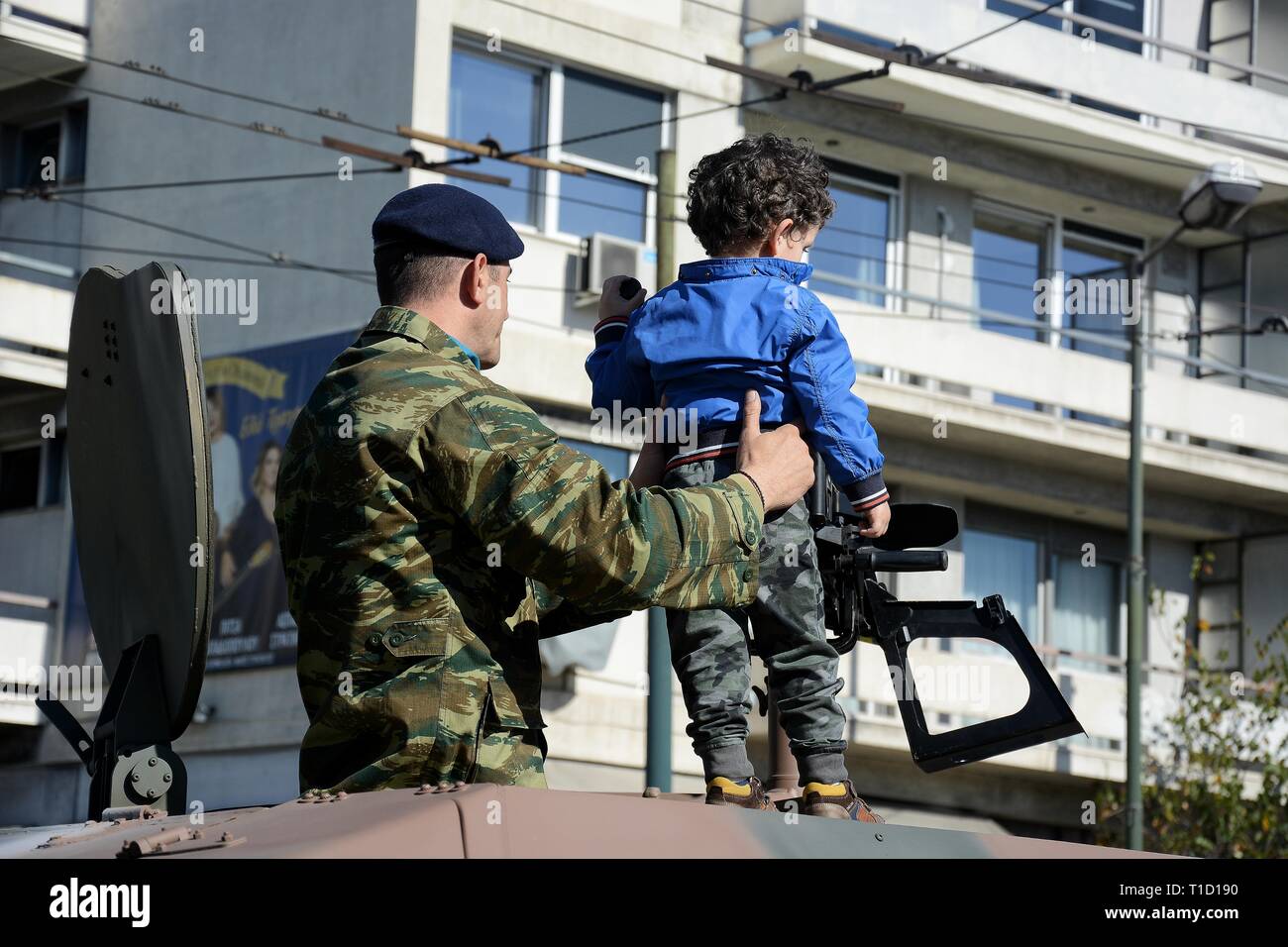 A member of Greek army seen holding a boy on top of an Armoured vehicle before the Military parade to commemorate the National Day in Athens. Stock Photo