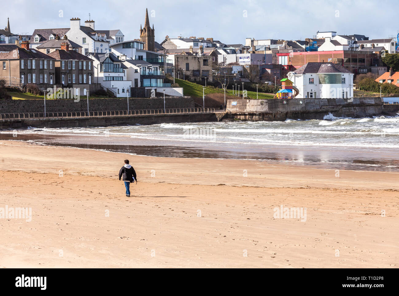 Portrush, Northern Ireland, UK - March 11, 2019: A lone figure walking on East Strand Beach on a blustery March day Stock Photo