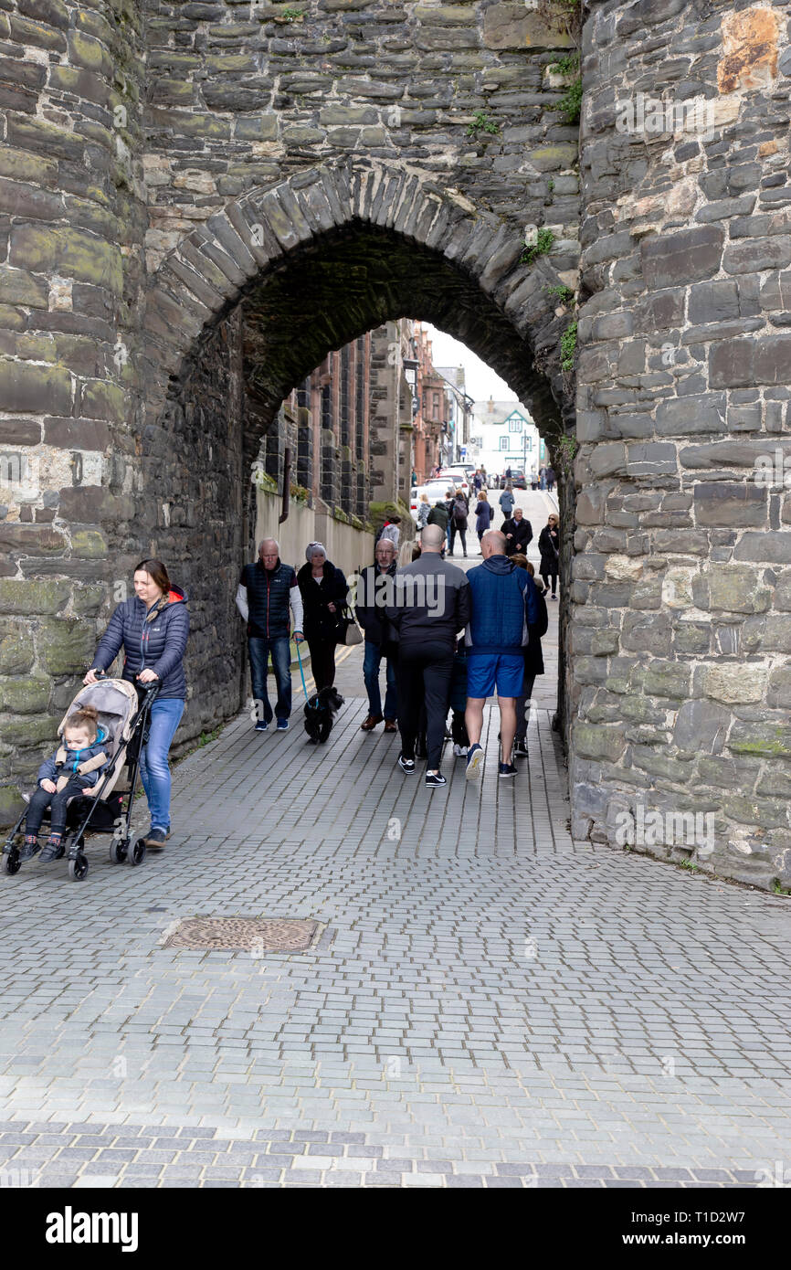 Tourists and locals passing through the old wall arch on Conwy Quay in North Wales which leads from the quay at Lower Gate Street to the High Street Stock Photo