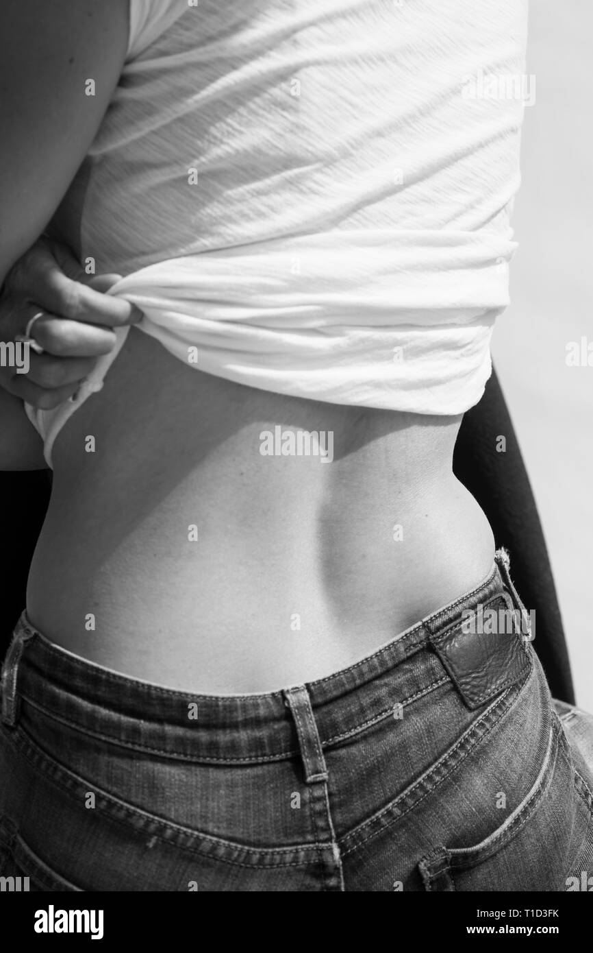 Rear View of Woman in Jeans Lifting her Shirt to Expose her Lower Back Stock Photo