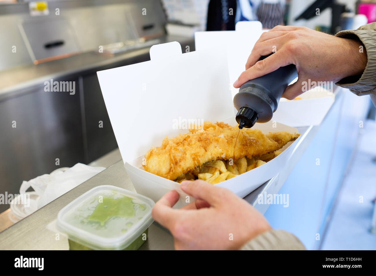 A man puts malt vinegar on top of his fish and chips at No1 Fish & Chips Shop in Cromer, North Norfolk, England. Stock Photo