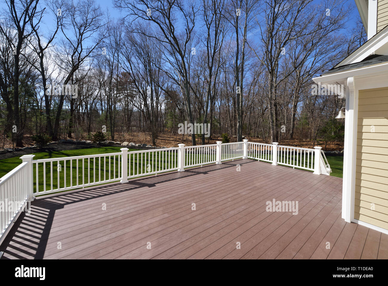 New backyard deck. White vinyl railings and composite brown boards. Large patio and garden space with a view to the woods. Stock Photo