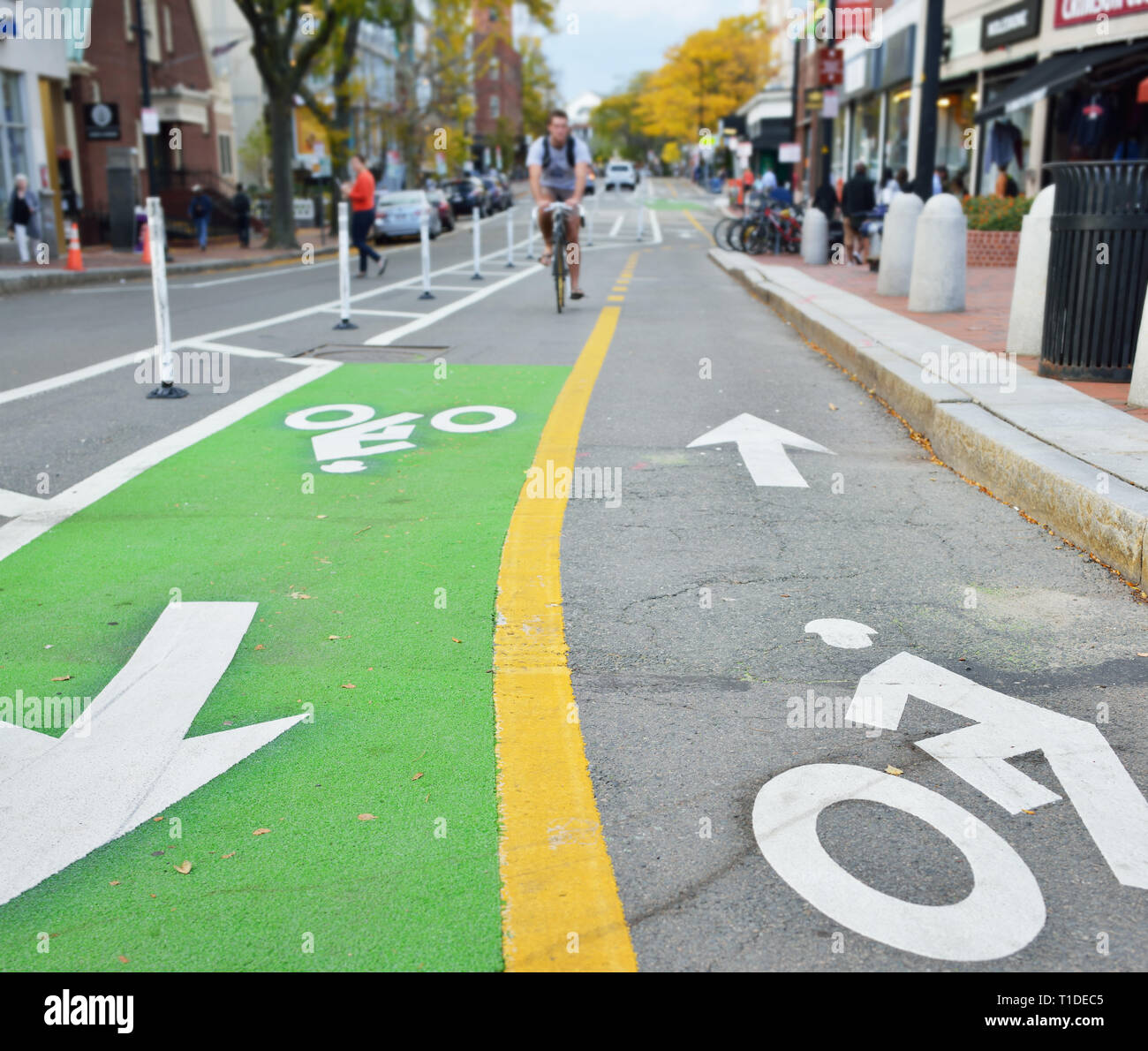 Two-way protected bike lane. Painted pavement markers in green, yellow and white. Biker and people walking on city street Stock Photo