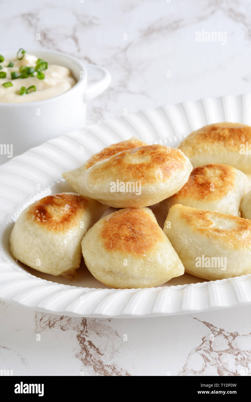 pile of pierogies with sour cream and spring onions on a platter Stock Photo