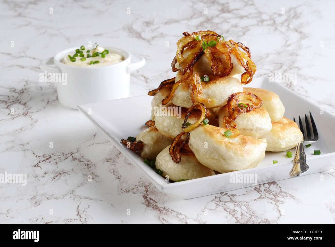pile of pierogies with sour cream caramelized onions and a fork Stock Photo