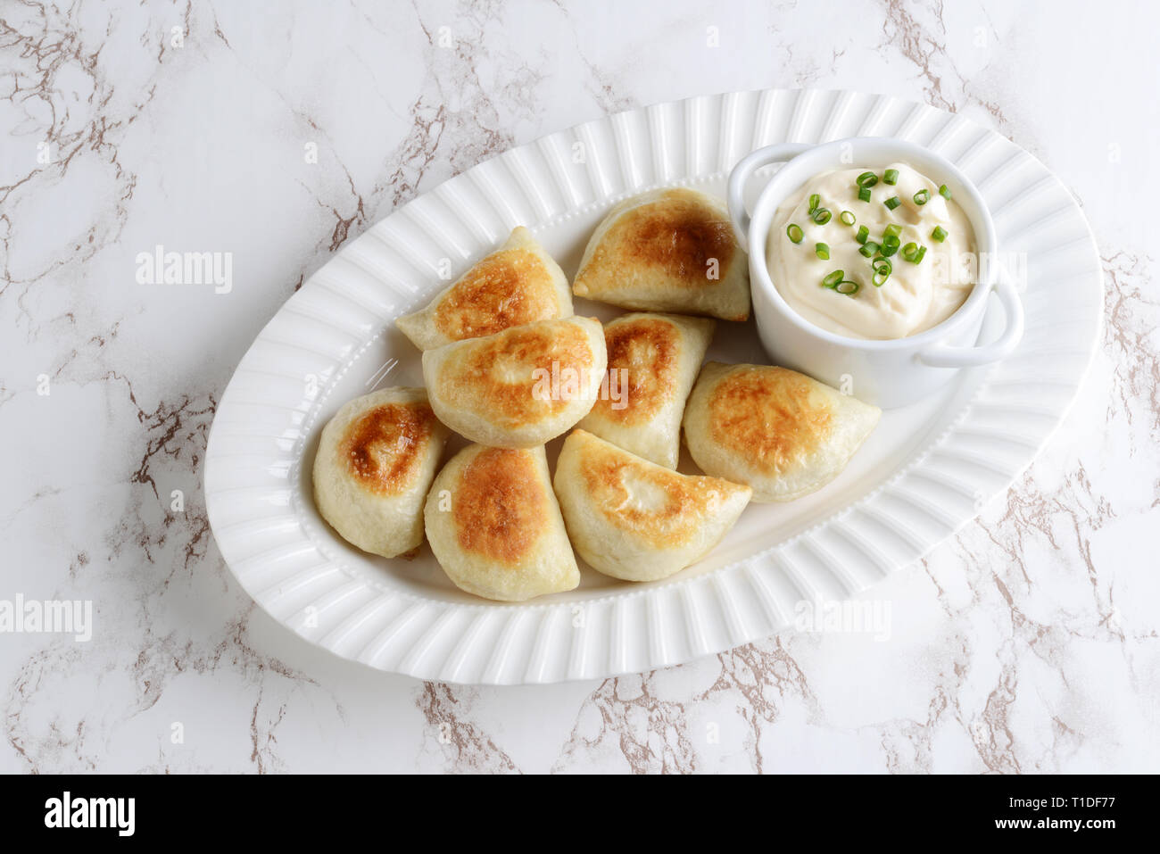 top view pierogies on a white platter with sour cream and spring onions Stock Photo