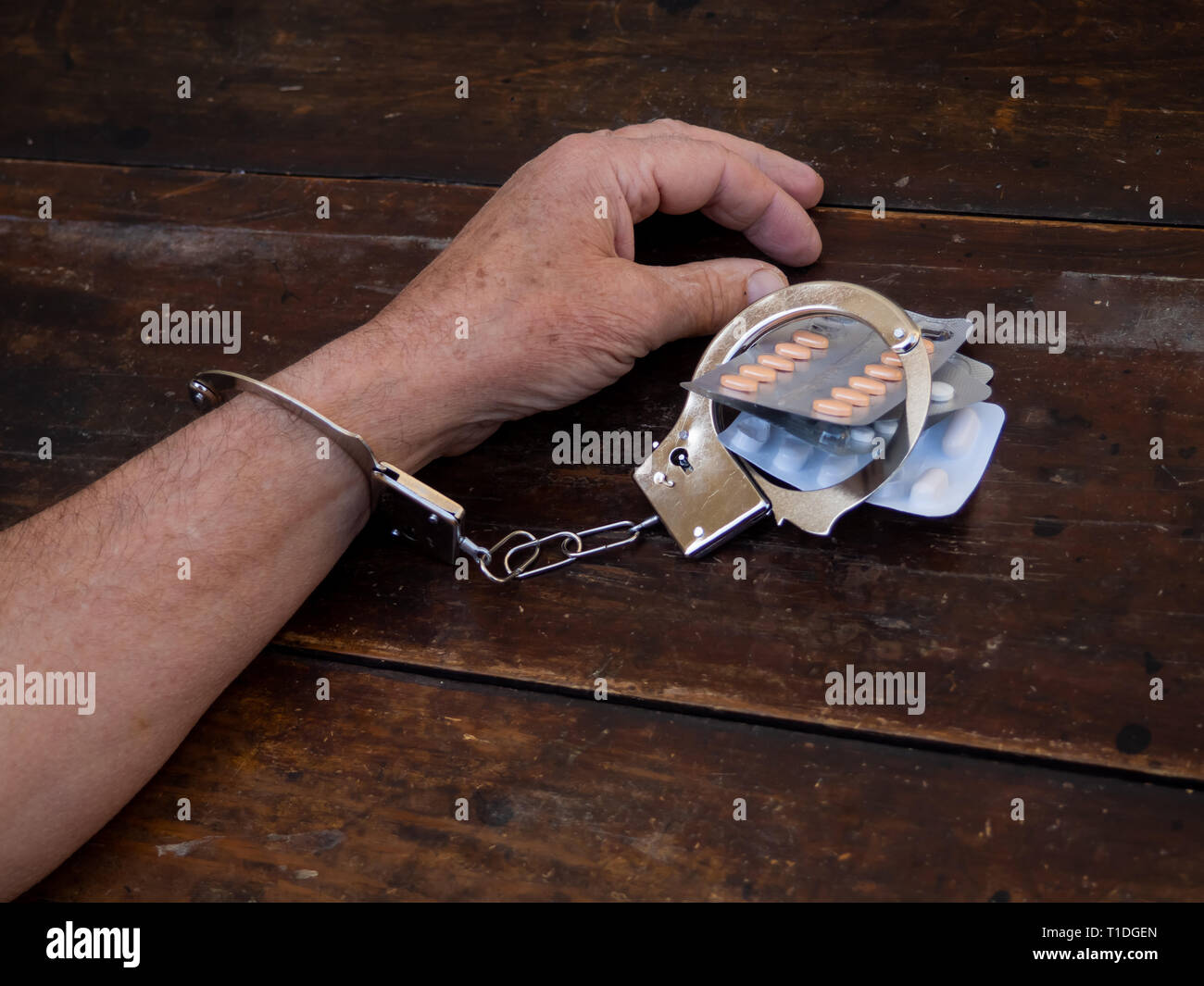 A man handcuffed to a handful of pills tablets. Drug addiction concept Stock Photo