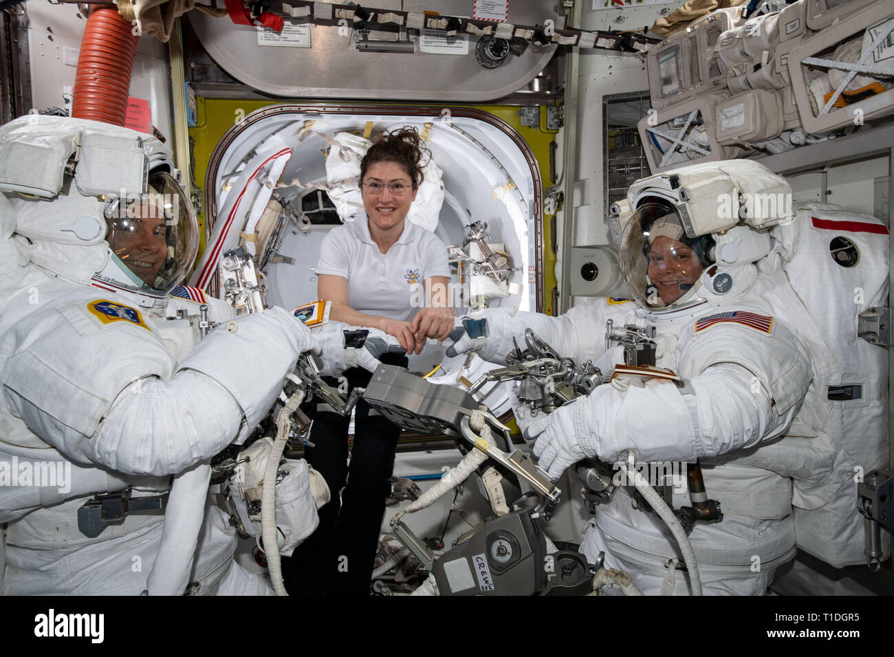 NASA astronaut Christina Koch, center, assists Nick Hague, left, and Anne McClain, right, with their U.S. spacesuits at the Quest Airlock before they begin their spacewalk to upgrade the space station power system March 22, 2019 in Earth Orbit. Stock Photo