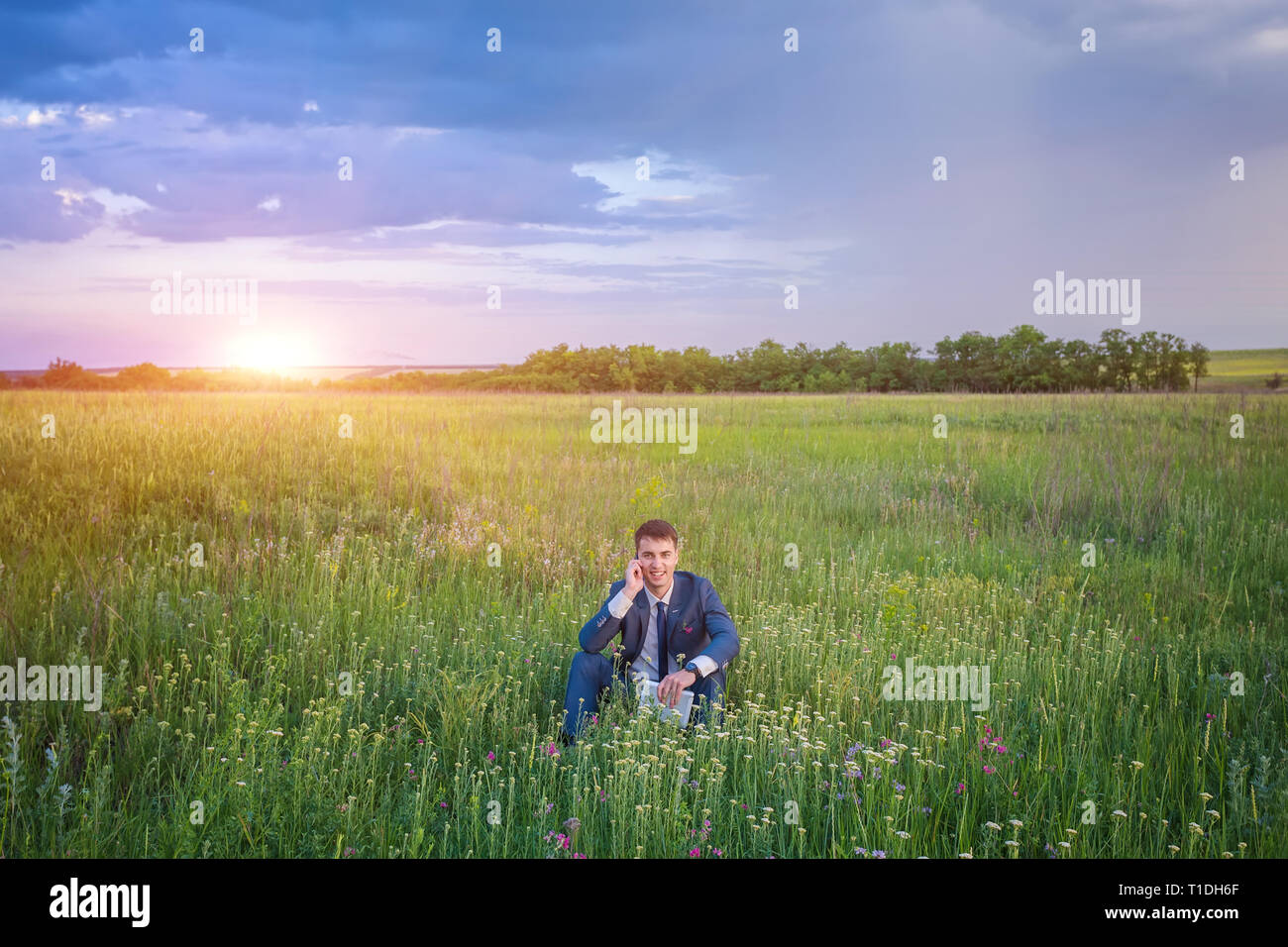 Businessman Sitting In His Suit On A Green Sunny Field Under A Blue Sky 