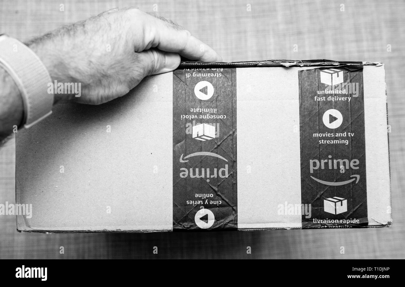 Paris, France - Jun 11, 2018: Man hand holding cardboard box with Amazon Prime logotype and sealed scotch tape fast delivery e-commerce parcel black and white Stock Photo
