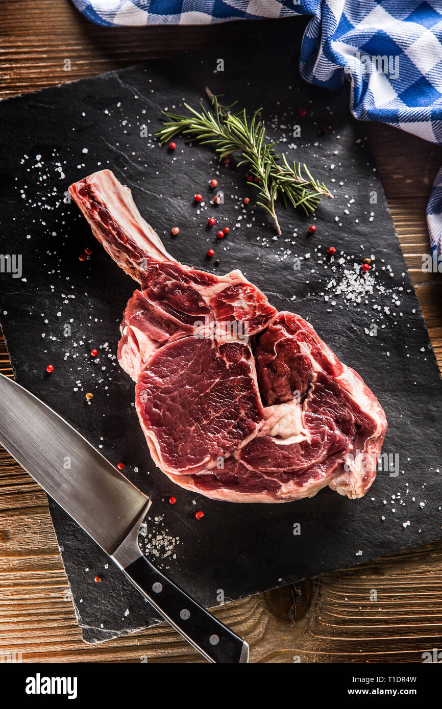 Raw beef tomahawk steak with salt pepper and rosemary on slate plate. Stock Photo