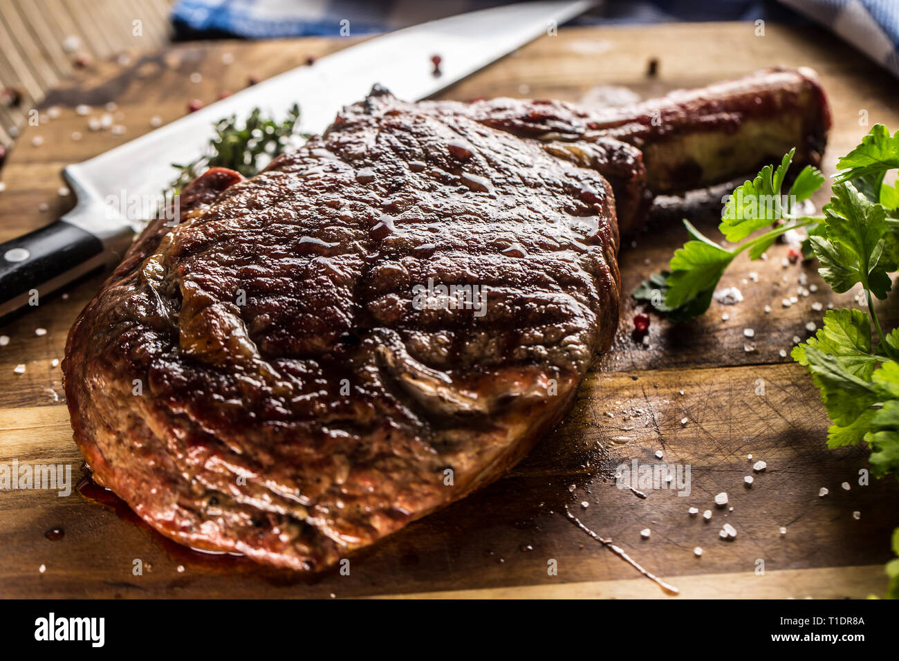 Freshly grilled tomahawk steak on slate plate with salt pepper rosemary and parsley herbs. Stock Photo