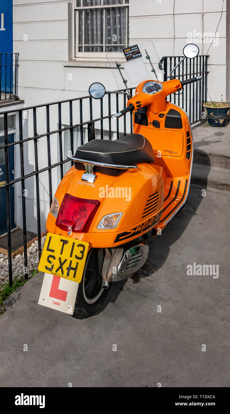 Scooters Rear View Close up Rear view of a Bright orange motor scooter parked outside a ...