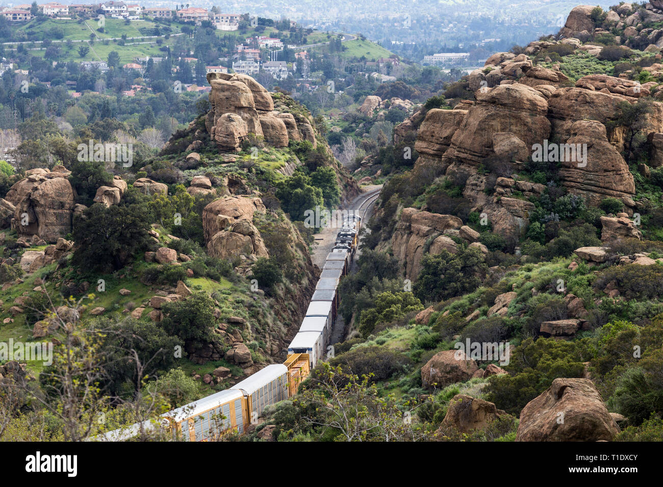 Los Angeles, California, USA - March 20, 2019:  Freight train passing rock formations and expensive San Fernando Valley homes in the Santa Susana Pass Stock Photo
