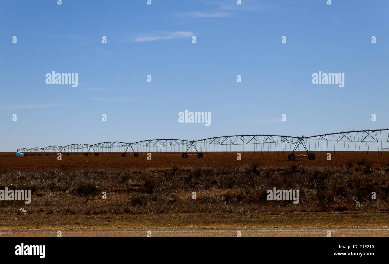Field irrigated a pivot irrigation system line with sprinklers watering a large field of crops Stock Photo