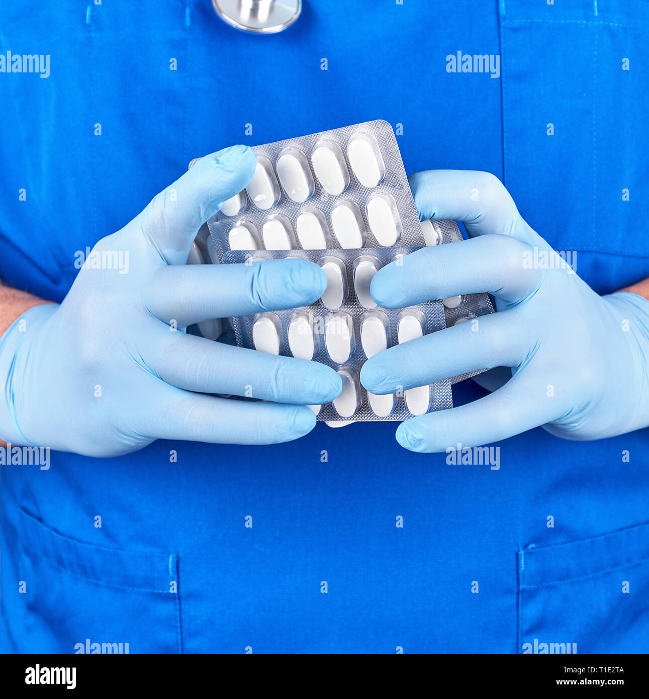 doctor in blue uniform and sterile gloves holding white pills in pack, close up Stock Photo