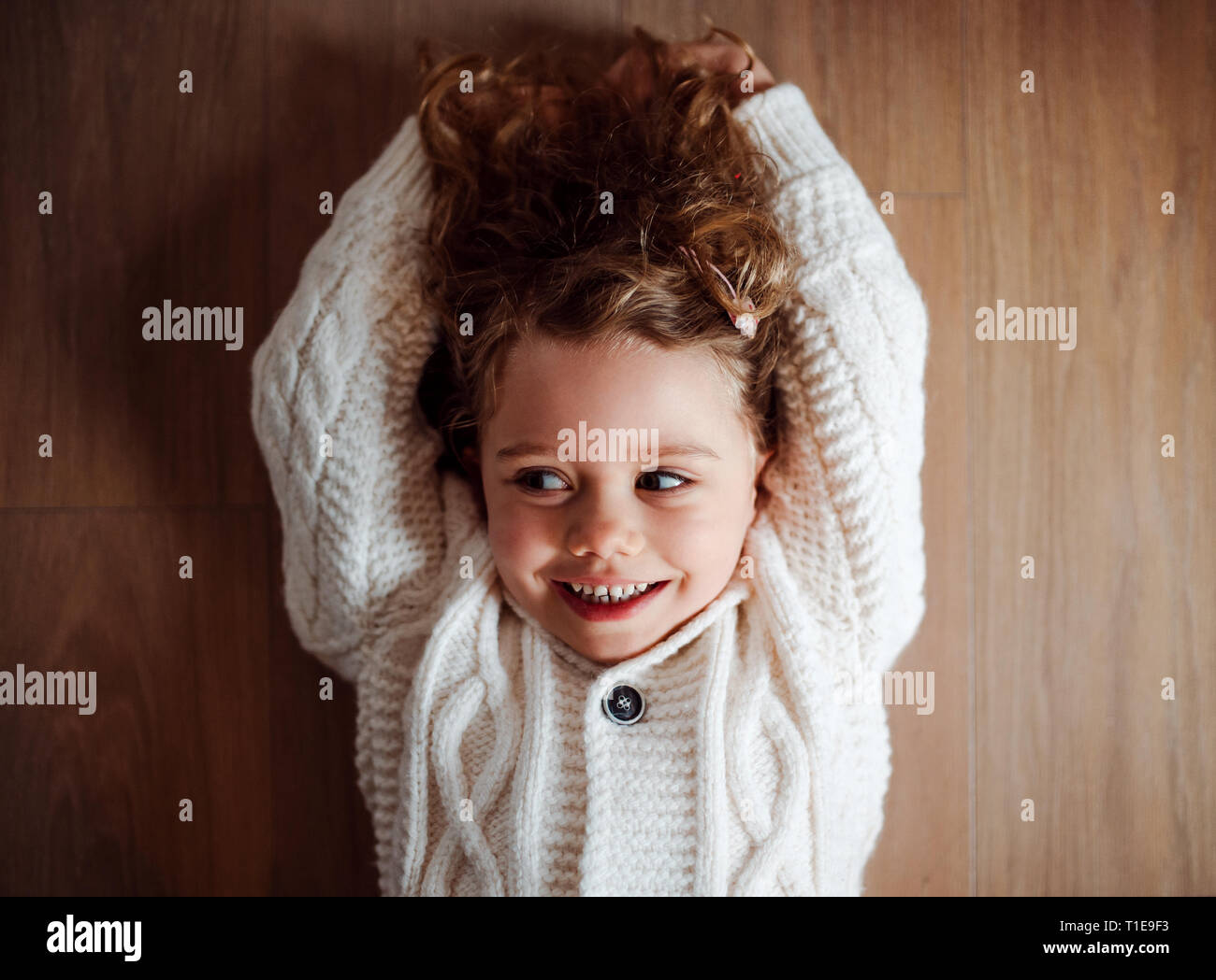A portrait of small girl with white knitted sweater lying on the floor ...