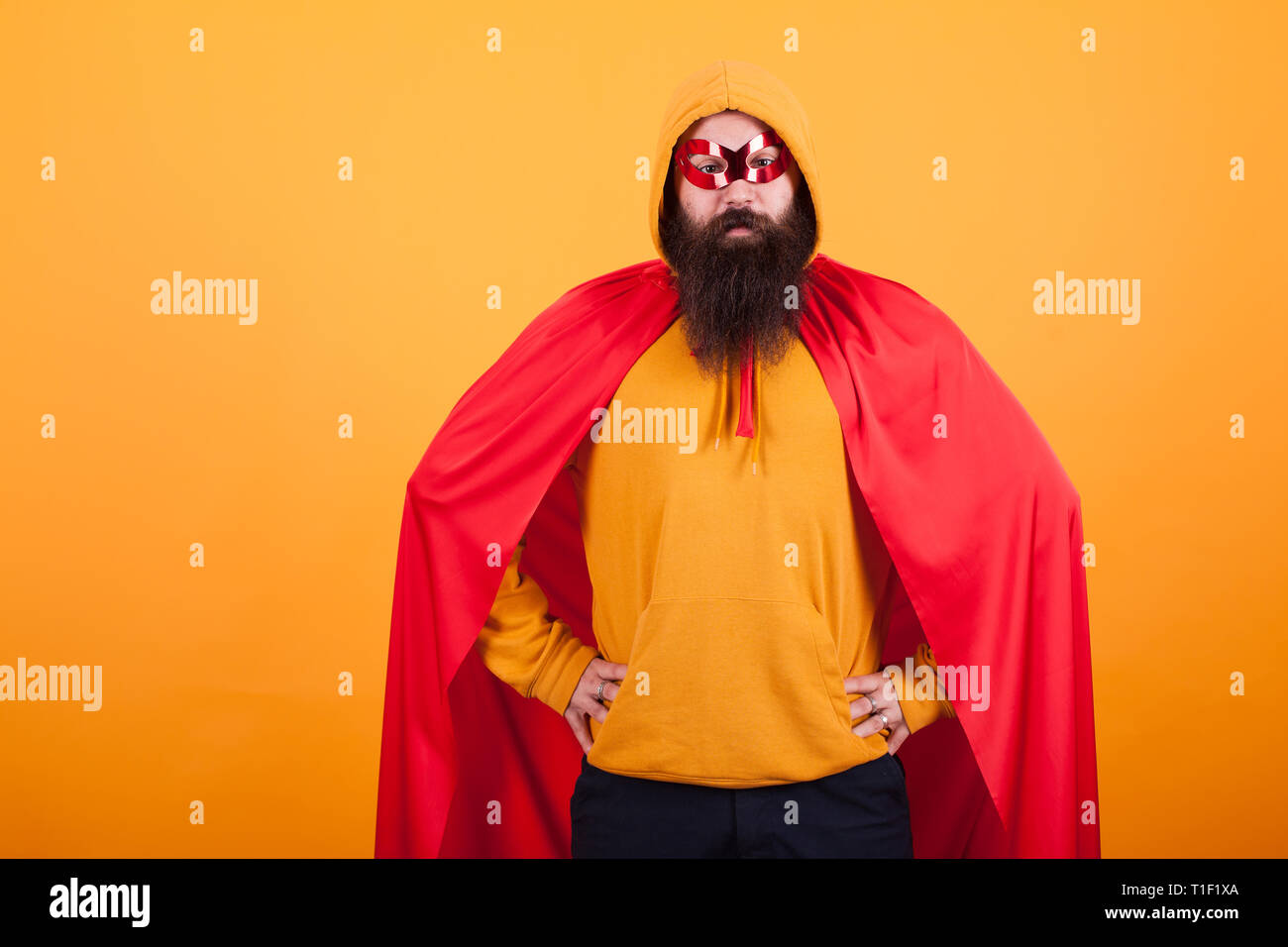 Handsome bearded man in superhero costume standing proudly over yellow background. Super power. Red cape. Long beard. Stock Photo