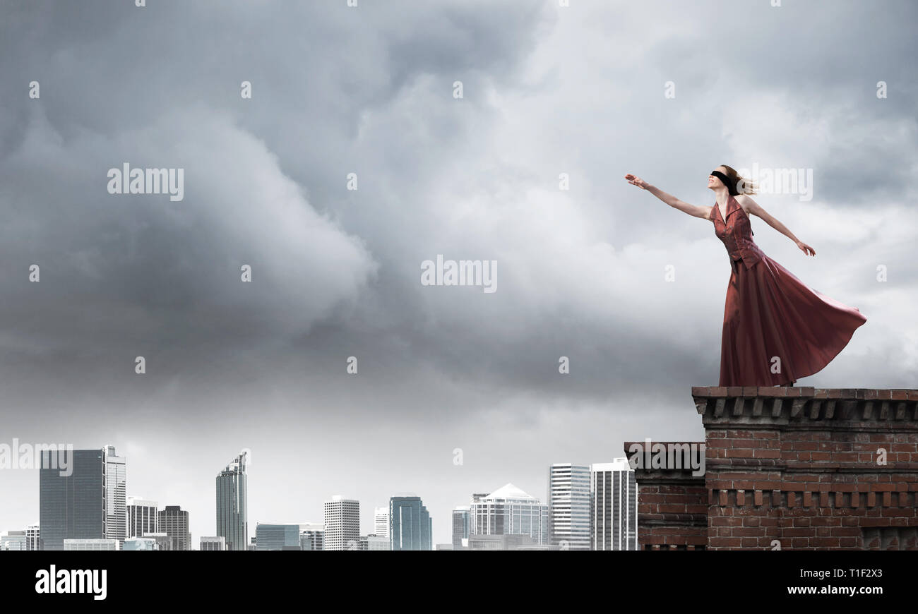 Blind woman in long red dress at top of building. Mixed media Stock Photo