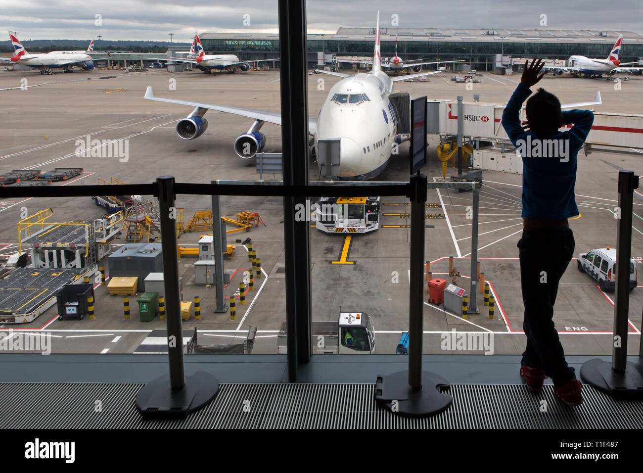 HEATHROW - A boy stares at the landing strip and a British Airways airplane from the departure gate. Stock Photo