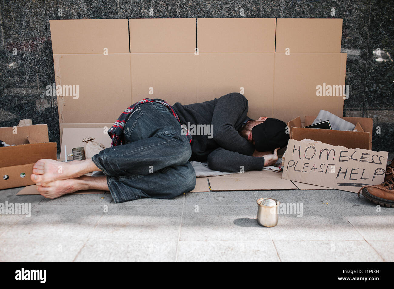 Helpless and defenceless man is lying on the cardboard on concrete