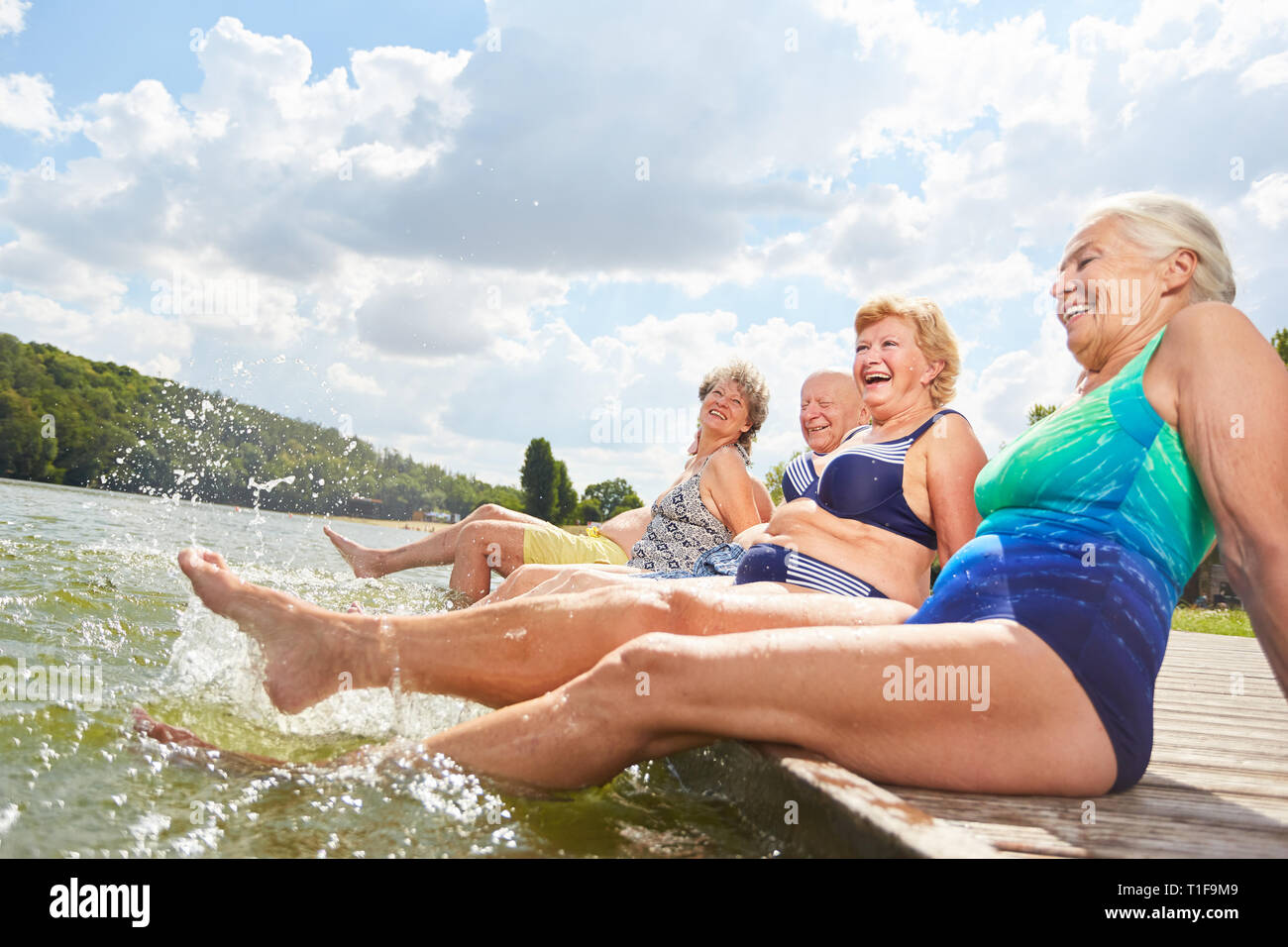 Active seniors splashing with their feet in the water during a summer vacation at the bathing lake Stock Photo