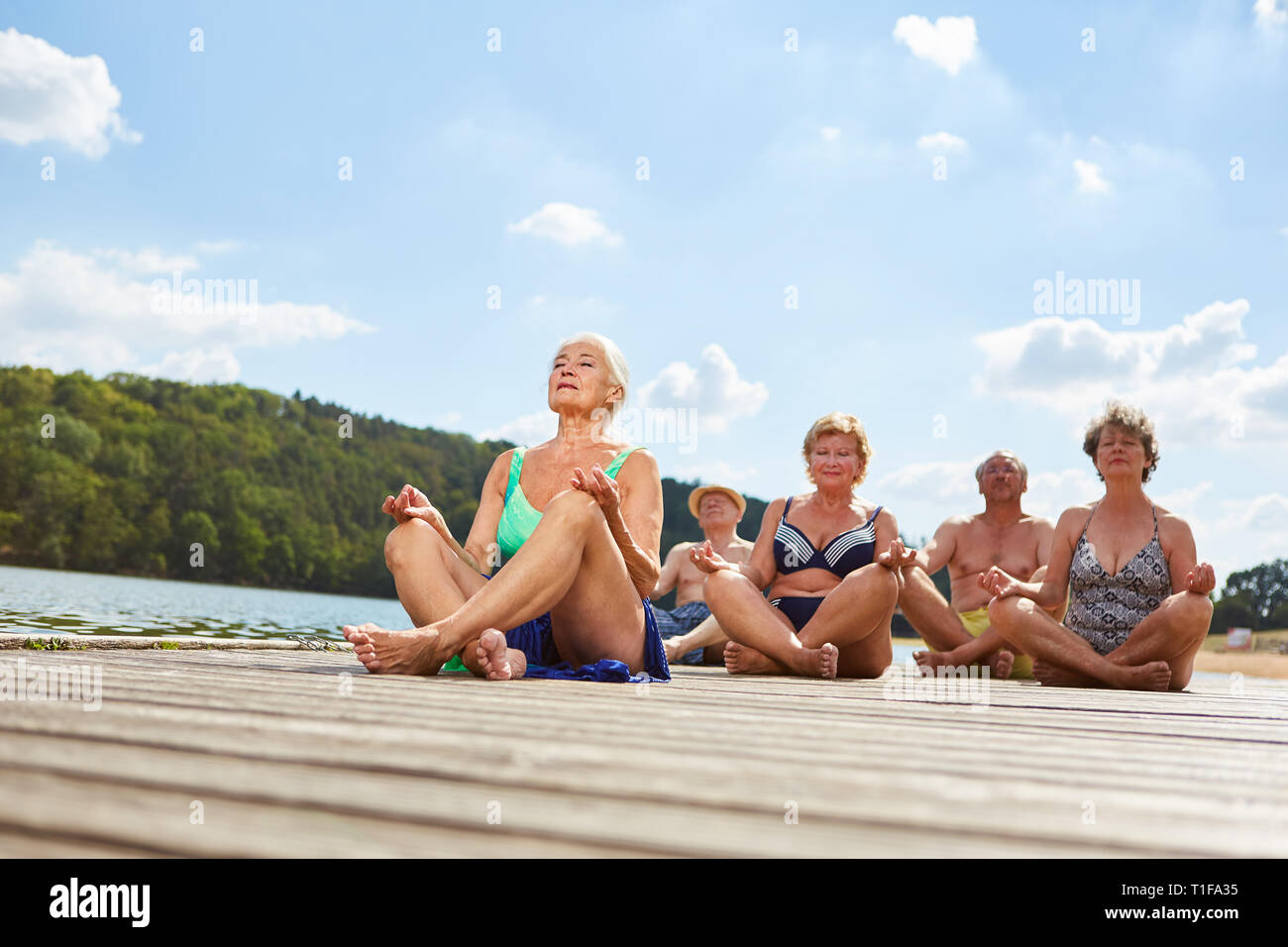 Group of seniors doing yoga exercise on the lake in summer for relaxation and health Stock Photo