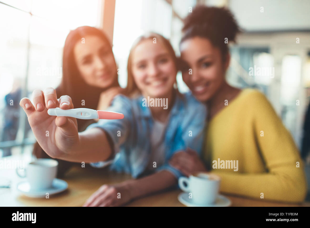 An intersting picture of trhee young girls where one of them is showing her pregnancy test with positive result to the camera. Looks like she is happy Stock Photo