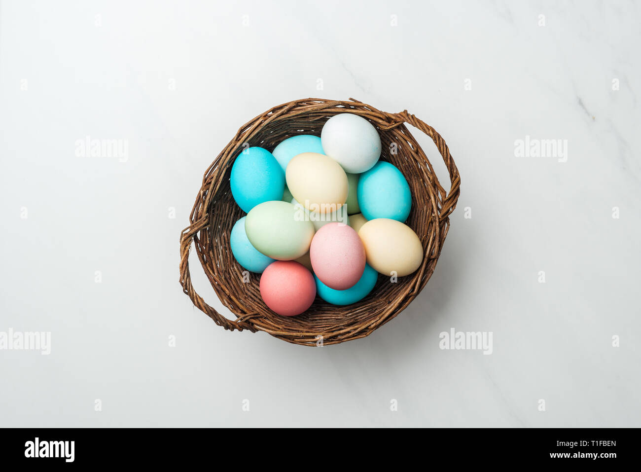 top view of colorful pastel easter eggs in wicker basket on white Stock ...