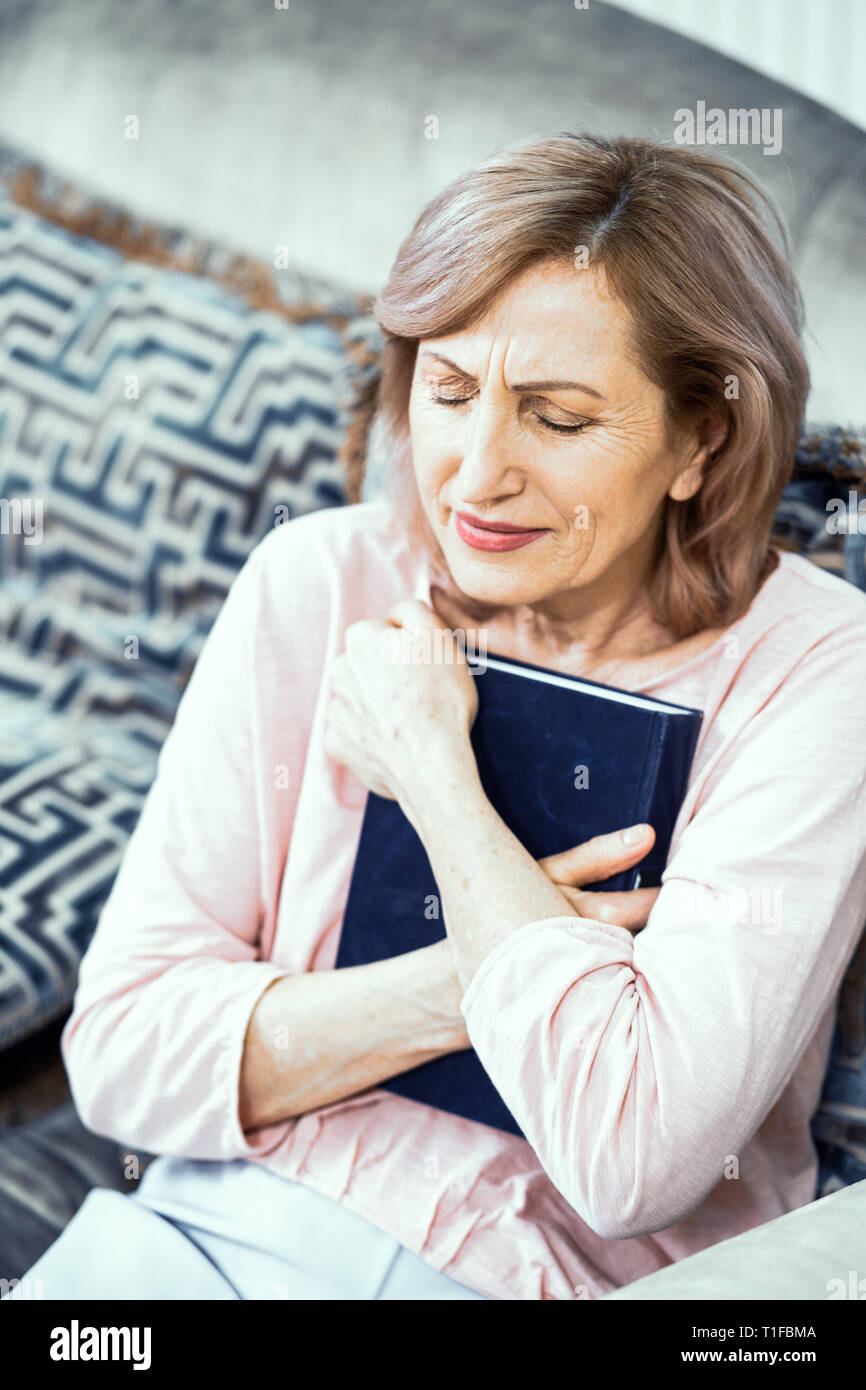 Middle Aged Woman Sitting On Sofa And Holding Bible Stock Photo