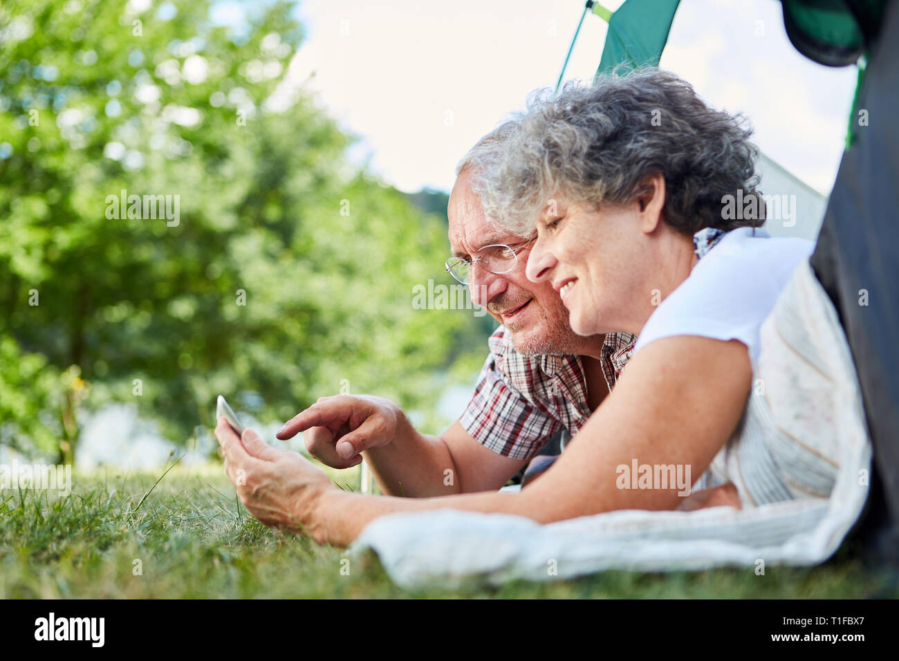 Senior couple using tablet computer online while camping at summer campsite Stock Photo