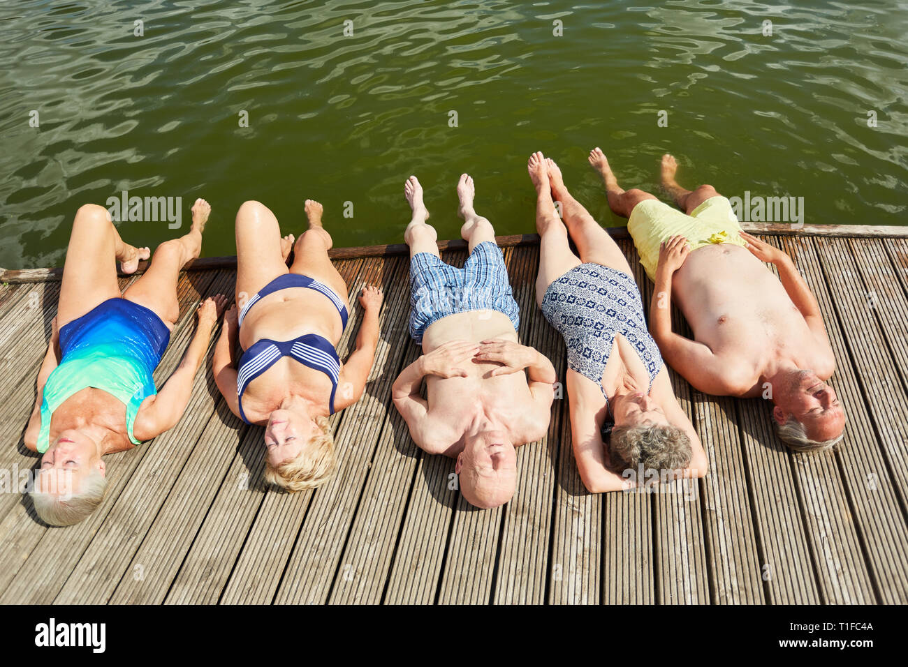 Group of seniors relaxing while sunbathing on a jetty at the lake on vacation Stock Photo