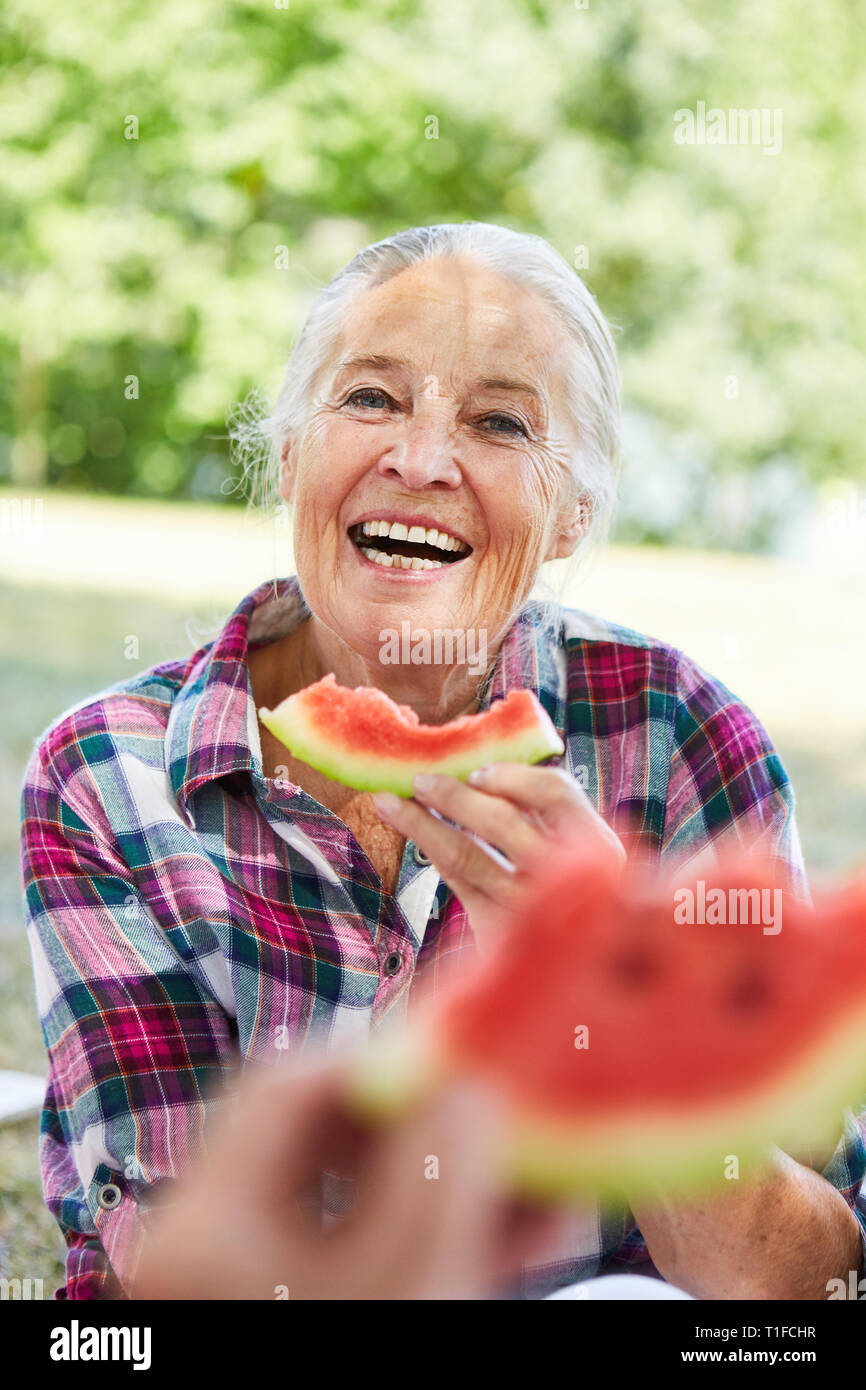 Cheerful senior woman eating melon at the park in summer on a trip Stock Photo