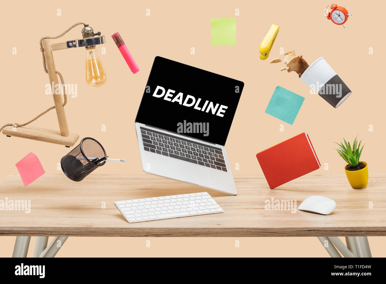 laptop with deadline lettering on screen, thermomug with coffee splash and stationery levitating in air above wooden desk isolated on beige Stock Photo