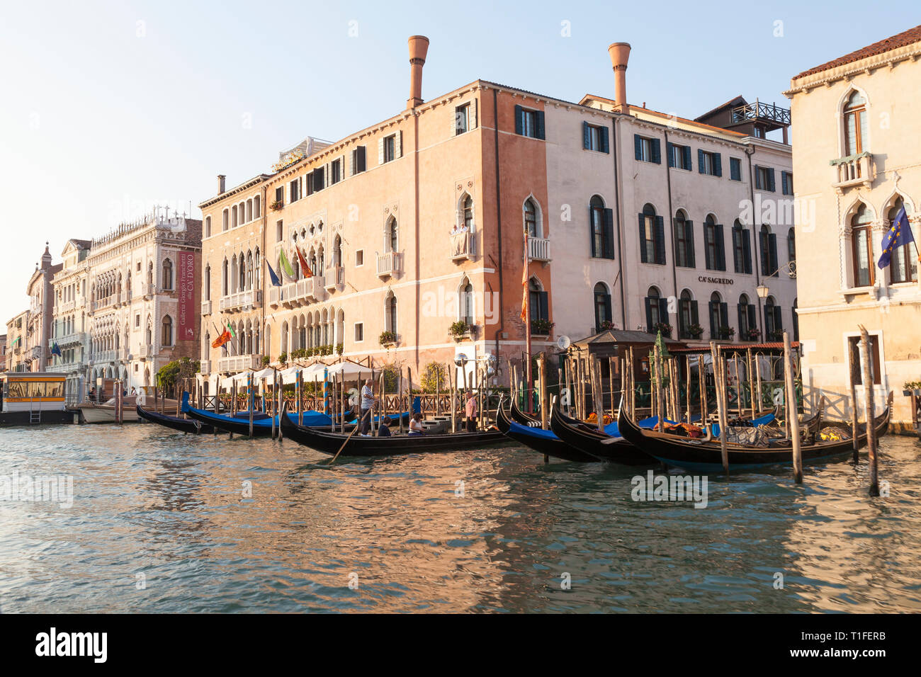 Ca' Sagredo Hotel and gondolas at Campo Santa Sofia, Grand Canal, Cannaregio, Venice, Veneto, Italy at sunset. Ca' d'Oro in background Stock Photo
