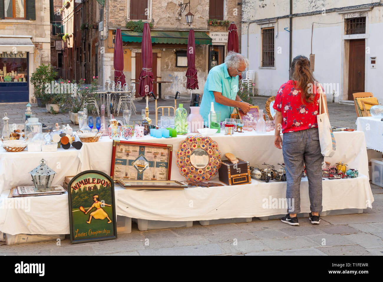Antiques market or Bric-a-Brac sale in campo dei Frari, San Polo, Venice, Veneto, Italy with open air tables early morning. Dealer serving young woman Stock Photo