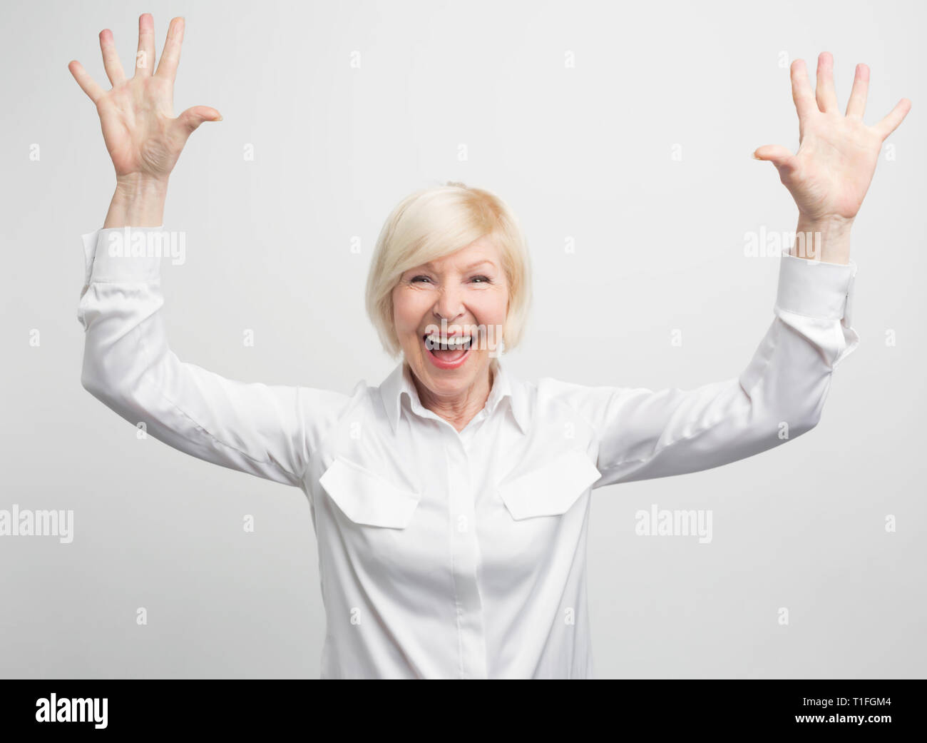 Beautiful and feminine old woman showing high-five with both hands. She is happy and surprised. This woman looks confident. Isolated on white Stock Photo