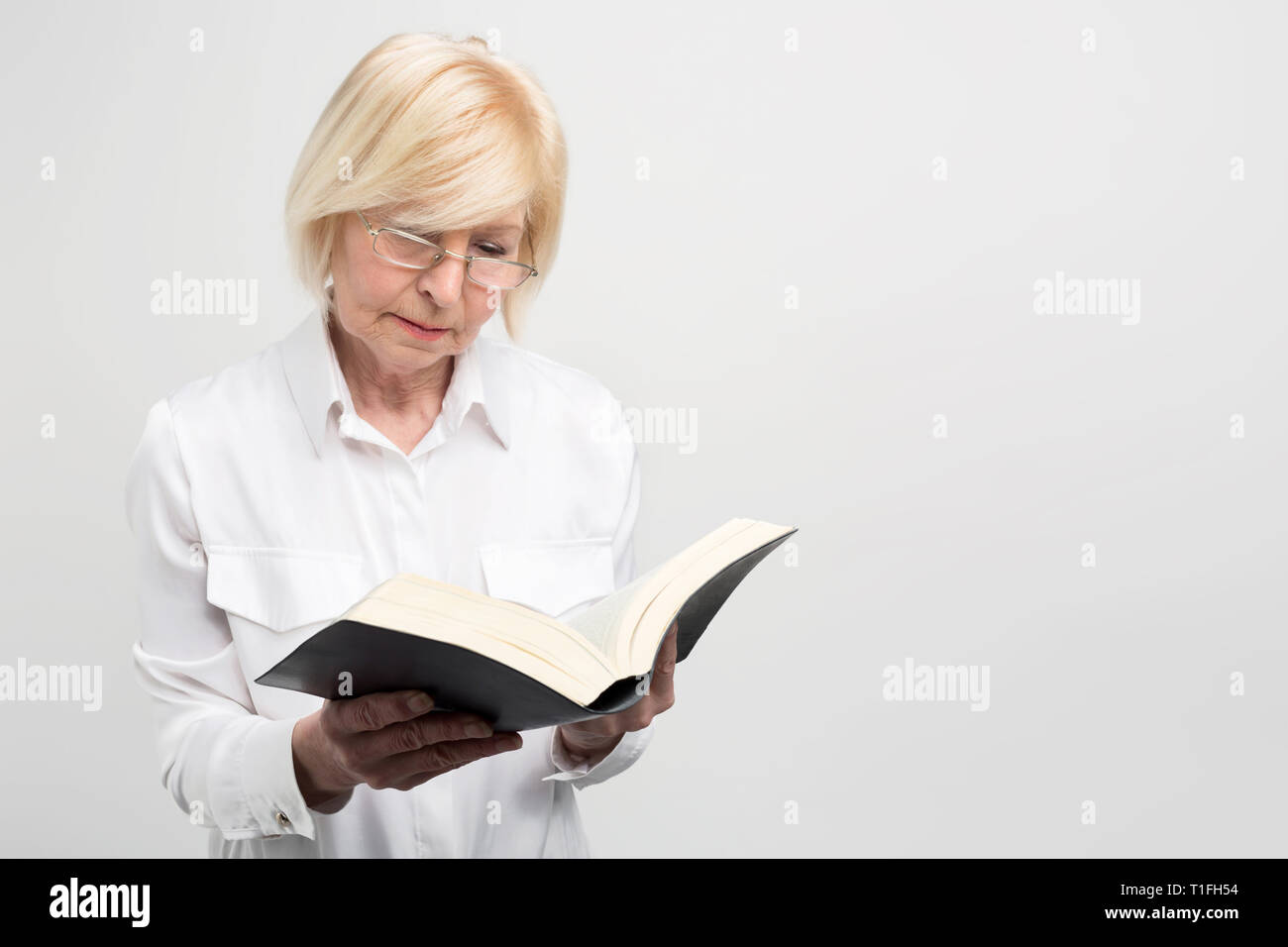 Senior business woman is standing in the room and reading a book. It is very interesting. Isolated on white background. Stock Photo
