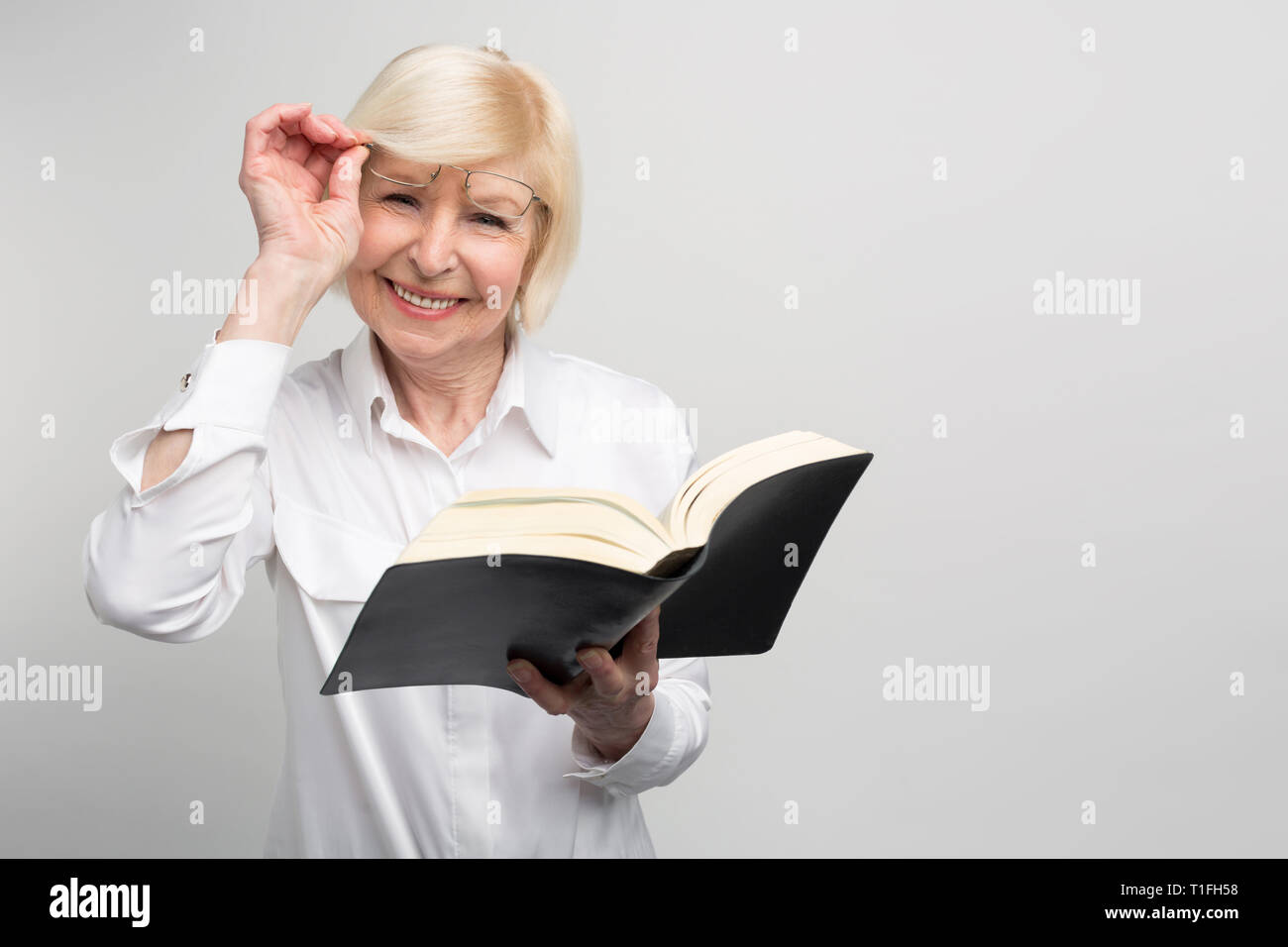 Senior woman is standing in the room and reading a book. She is trying to learn somethinf new at the retirement because she has a lot of good free Stock Photo