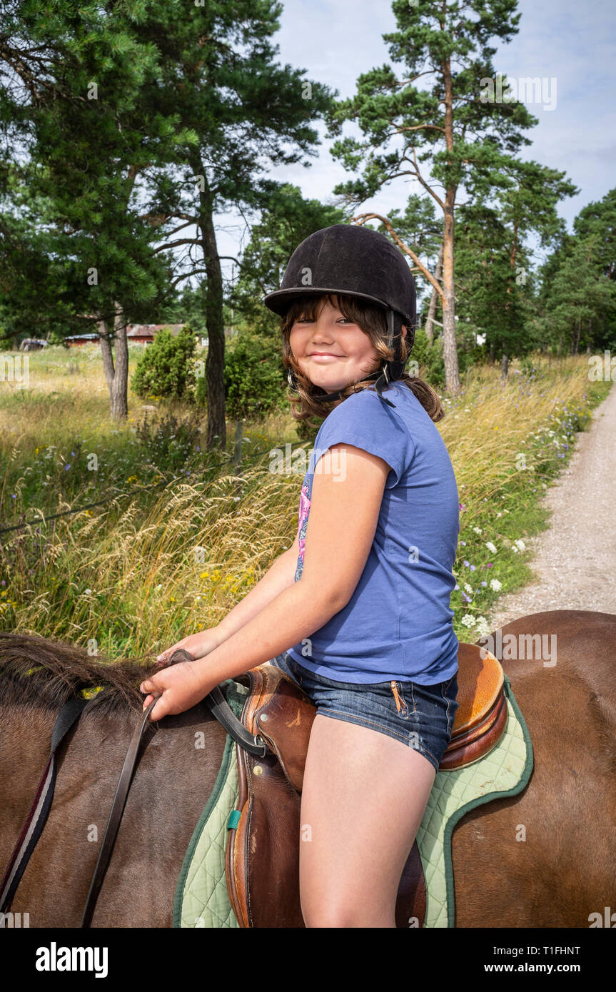 Young girl riding an a brown horse outdoors in the countryside, Gotland, Sweden, Scandinavia. Stock Photo