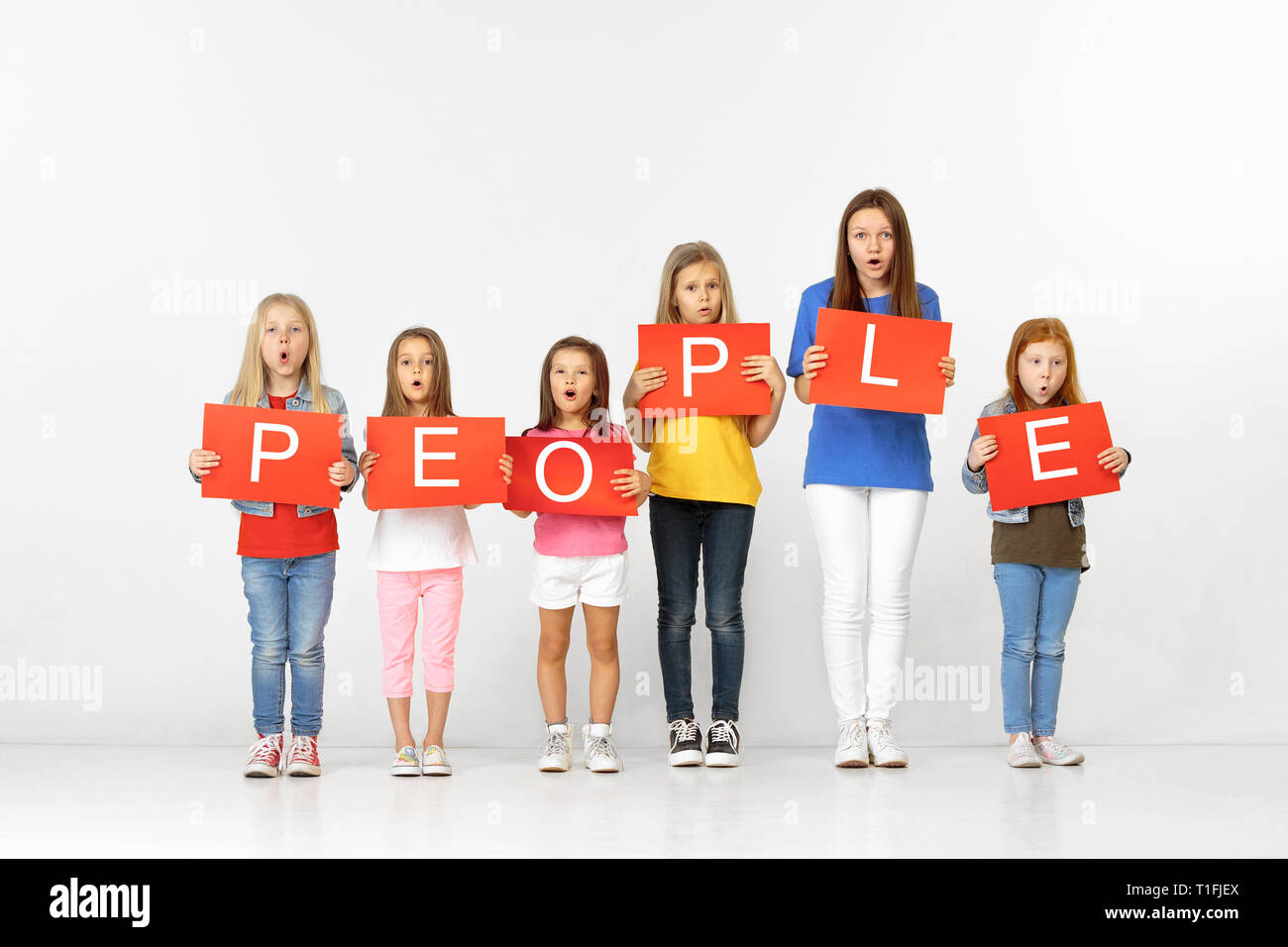 All people are bright. Group of astonished children with red banners making word isolated in white studio background. Education and advertising concept. Protest and children's rights concepts. Stock Photo