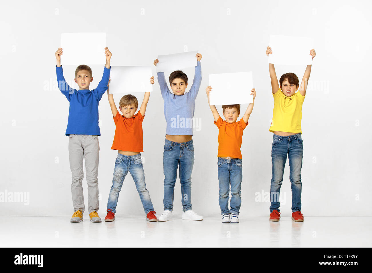 Group of angry children with a white empty banners isolated in studio background. Education and advertising concept. Protest and children's rights concepts. Stock Photo