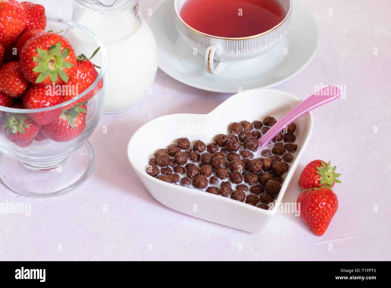 Breakfast for special little princess. Chocolate cereal balls, milk, strawberries and red fruit tea on pink backdrop Stock Photo