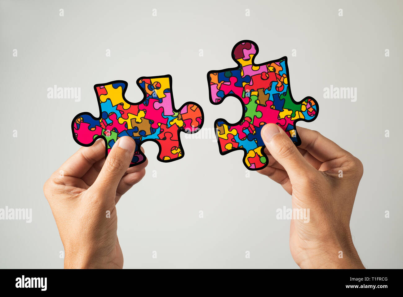 closeup of a man with two puzzle pieces patterned with many puzzle pieces of different colors, symbol of the autism awareness, on a white background Stock Photo