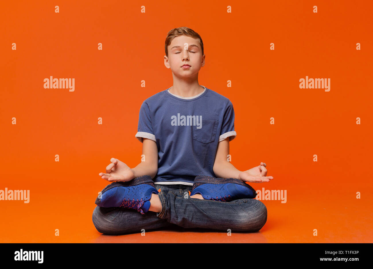 Calm boy sitting on floor and meditating in lotus position. Stock Photo