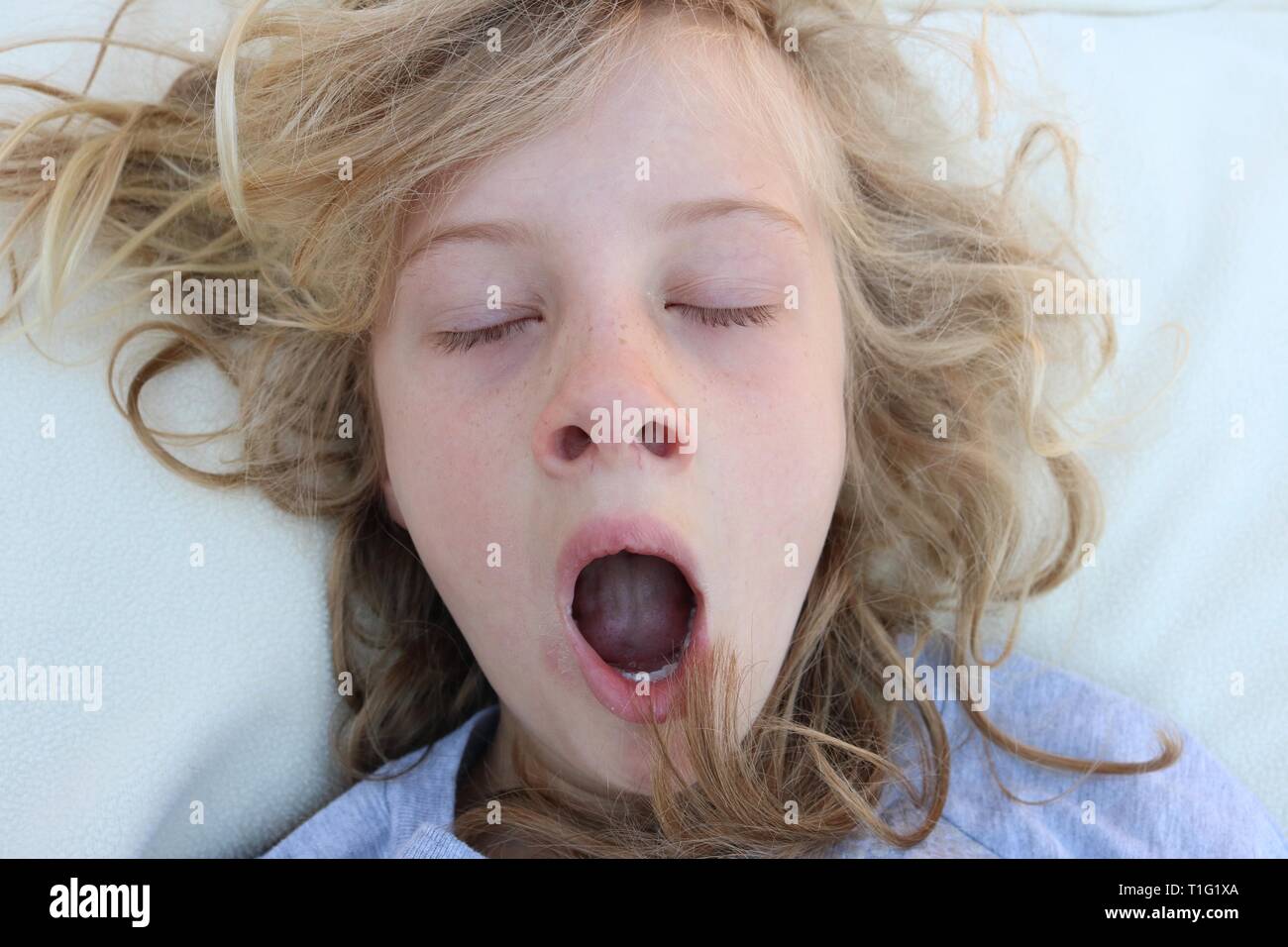 Girl with unruly blonde curls yawning and waking up with her eyes closed Stock Photo